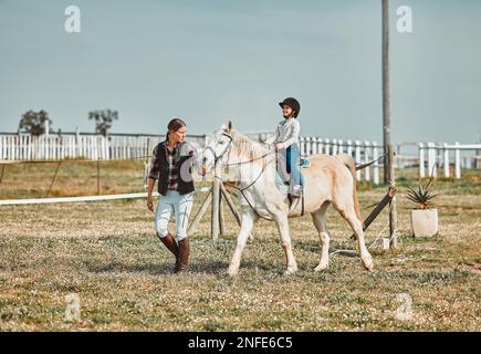 .Leçon, aide et femme avec un enfant sur un cheval pour l'apprentissage, le sport et le passe-temps sur une ferme en Italie. Aider, soutenir et encadrer l'enseignement d'une fille Banque D'Images