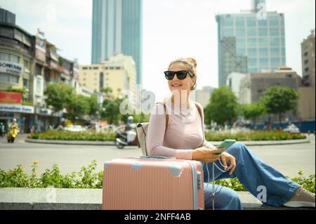 Joyeuse touriste avec un smartphone et une valise dans la rue Banque D'Images