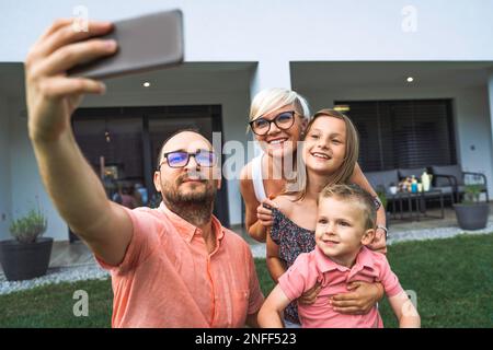 Père tenant un téléphone haut, prenant un selfie de toute la famille goofing autour de lui Banque D'Images