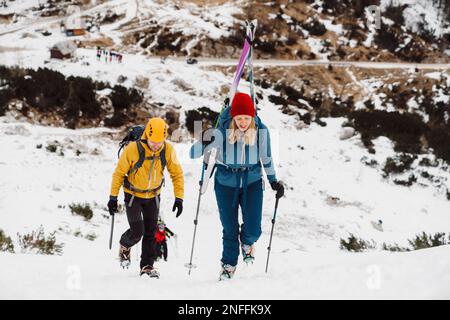 Couple de alpinistes grimpant sur une montagne enneigée, femme portant des skis sur son dos Banque D'Images