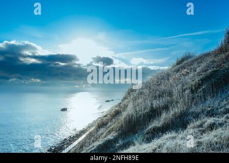 Froid, tôt le matin vue d'une falaise en pente recouverte de gel. Une tempête de neige lointaine est vue à l'horizon, en mer. Banque D'Images