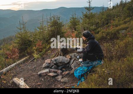 Randonnée en plein air dans la nature passionnée assis près d'un feu de camp en appréciant le petit déjeuner au lever du soleil. Petit déjeuner et prendre de la vitamine D au sommet de la colline. T Banque D'Images