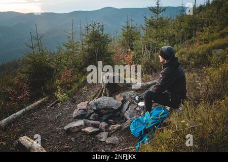 Randonnée en plein air dans la nature passionnée assis près d'un feu de camp en appréciant le petit déjeuner au lever du soleil. Petit déjeuner et prendre de la vitamine D au sommet de la colline. T Banque D'Images