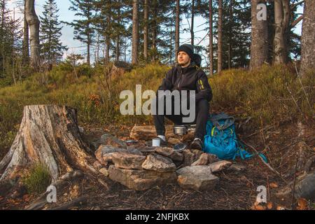 Randonnée en plein air dans la nature passionnée assis près d'un feu de camp en appréciant le petit déjeuner au lever du soleil. Petit déjeuner et prendre de la vitamine D au sommet de la colline. T Banque D'Images