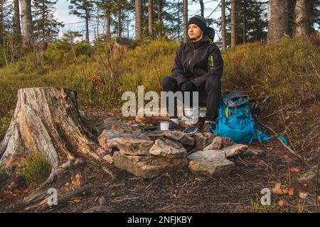 Randonnée en plein air dans la nature passionnée assis près d'un feu de camp en appréciant le petit déjeuner au lever du soleil. Petit déjeuner et prendre de la vitamine D au sommet de la colline. T Banque D'Images