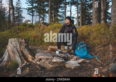 Randonnée en plein air dans la nature passionnée assis près d'un feu de camp en appréciant le petit déjeuner au lever du soleil. Petit déjeuner et prendre de la vitamine D au sommet de la colline. T Banque D'Images