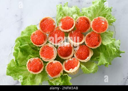 Tartelettes au beurre et caviar rouge. Assiette avec hors-d'œuvre caviar décorée de feuilles de laitue sur fond clair Banque D'Images