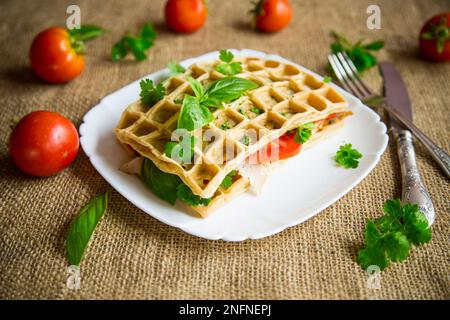 Sandwich de deux omelettes aux œufs avec bacon et tomates à l'intérieur, en forme de gaufre. Banque D'Images