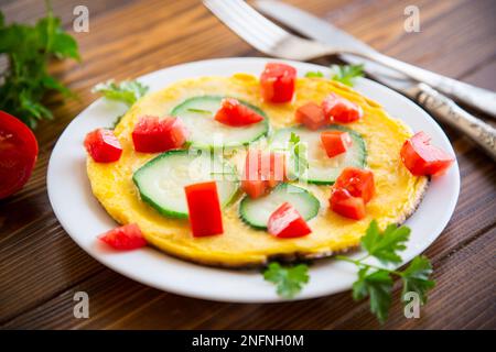 Omelette frite avec courgettes, tomates, herbes dans une assiette sur une table en bois. Banque D'Images