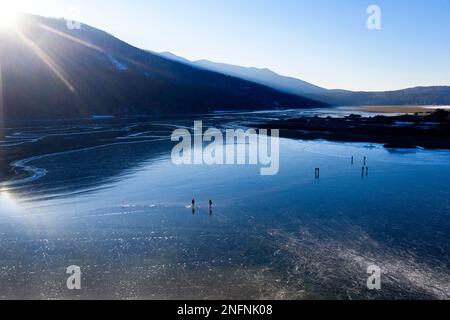 Les gens patinent dans la nature sur un beau lac naturel gelé Cerknica à la fin d'une journée d'hiver ensoleillée et froide, la Slovénie Banque D'Images