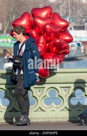 Personne qui vend des ballons rouges en forme de coeur après la Saint Valentin sur le pont de Westminster, Londres, Royaume-Uni Banque D'Images