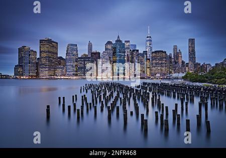 Grumes en bois dans la rivière est et les gratte-ciel de Lower Manhattan à l'heure bleue, photo de New York en exposition prolongée, vue depuis le Brooklyn Bridge Park Banque D'Images