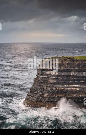 Pêcheur debout au bord des hautes falaises de Downpatrick Head avec des vagues écrasant à l'aube. Lever de soleil spectaculaire avec ciel nuageux, Mayo, Irlande Banque D'Images