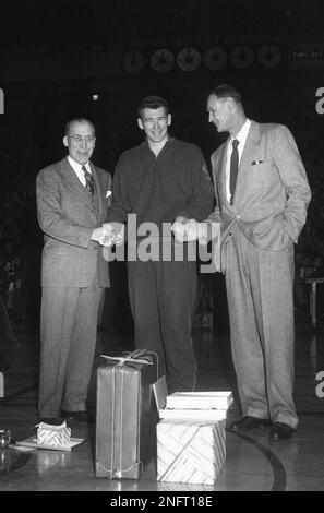 Ernie Vandeweghe, center, onetime Colgate star who is completing his fourth season with New York Knicker-Bockers pro basketball team, shakes hands with Colgate coach Karl Lawrence, left, and Knick's coach Joe Lapchick, right, at ceremony honoring Ernie before Knicks-Boston Celtics game on March 8, 1953 in New York's Madison Square Garden. In the view are some of gifts Vandeweghe received from his neighbors at Oceanside, Lon Island, and from Colgate alumni and fans. (AP Photo/JL)