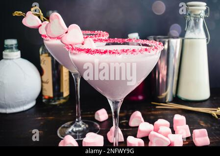 Cocktail de Saint-Valentin framboise et chocolat blanc : cocktail rose dans un verre martini bordé de saupoudriers et garni de guimauves en forme de coeur Banque D'Images