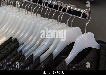 Une rangée de cintres en plastique blanc dans un magasin avec une veste tricotée marron accrochée à eux. Gros plan. Banque D'Images