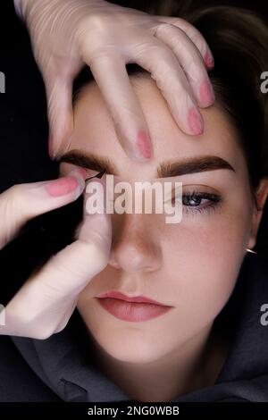 Maquillage permanent des sourcils, le maître tient le sourcil du modèle et effectue un maquillage permanent des sourcils Banque D'Images