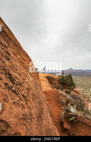 Femme randonneur se tenant sur le sentier Bell Rock dans les formations de roches rouges dans la forêt nationale de coconino à Sedona Arizona USA contre fond de nuages blancs. Banque D'Images