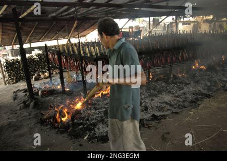 Un travailleur maintient la distribution de la combustion de noix de coco utilisée comme combustible pour fumer des viandes de thon listao dans une industrie domestique à Bitung, dans le nord de Sulawesi, en Indonésie. Selon la FAO, dans son dernier rapport (2022), l'Indonésie est le troisième producteur mondial de la production d'animaux aquatiques dans le domaine de la pêche et de l'aquaculture. Cinq pays — la Chine, l'Inde, l'Indonésie, le Vietnam et le Pérou — sont responsables d'environ 58 pour cent de la production mondiale. L'Indonésie est également l'un des pays où les aliments aquatiques contribuent à la moitié ou plus de l'apport total en protéines animales, selon le rapport. Banque D'Images
