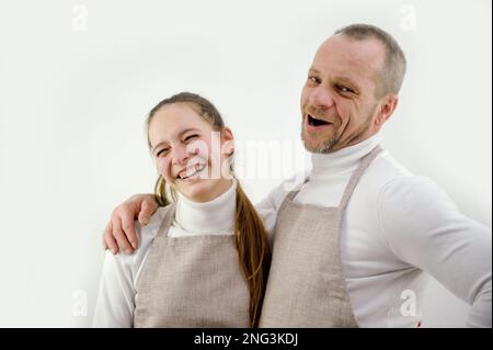 Couple aimant heureux préparant le dîner dans la cuisine moderne ensemble, embrassant, debout à table, souriante jeune femme portant un tablier coupant des légumes pour la salade, les conjoints appréciant le temps libre Banque D'Images