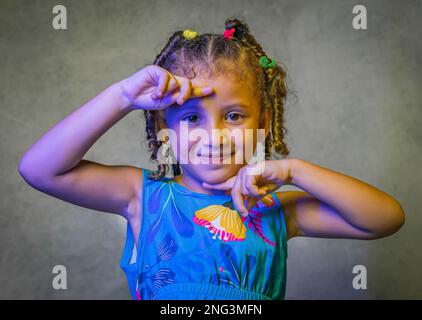 Studio portrait de belle petite fille dans la belle robe bleue sur fond violet, fille brésilienne souriant, donnant des baisers et faisant des visages drôles Banque D'Images
