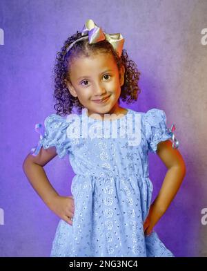 Studio portrait de belle petite fille dans la belle robe bleue sur fond violet, fille brésilienne souriant, donnant des baisers et faisant des visages drôles Banque D'Images