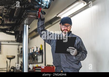 Prise de vue moyenne. Un ouvrier d'atelier de réparation regardant son bloc-notes et tenant une main avec un outil. Photo de haute qualité Banque D'Images