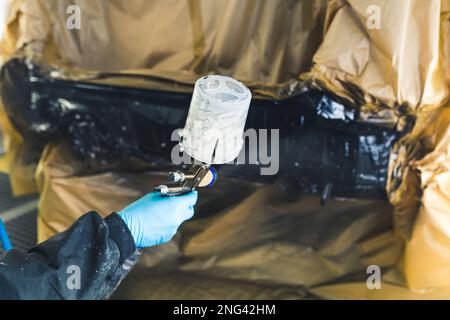 Mécanicien automobile portant des gants peignant une voiture dans un atelier de réparation automobile refinissage de voiture. Photo de haute qualité Banque D'Images