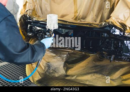 Mécanicien automobile portant des gants peignant une voiture dans un atelier de réparation à l'aide d'un aérographe. Photo de haute qualité Banque D'Images