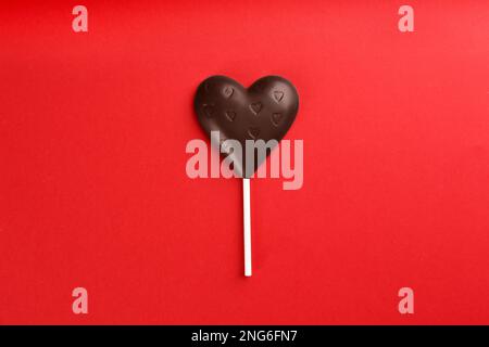 Lollipop en forme de coeur de chocolat sur fond rouge, vue du dessus Banque D'Images