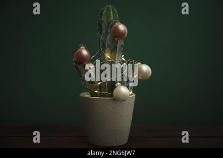 Magnifique cactus avec boules de Noël et lumières festives sur table en bois sur fond vert Banque D'Images