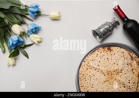 Savoureux matzos, vin et tulipes sur fond gris clair, plat avec espace pour le texte. Fête de la Pâque (Pesach) Banque D'Images
