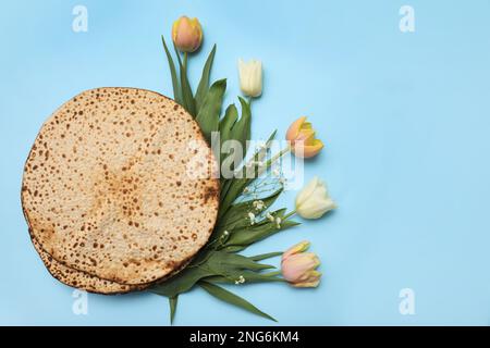 Savoureux matzos et fleurs fraîches sur fond bleu clair, plat. Fête de la Pâque (Pesach) Banque D'Images