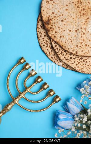 Savoureux matzos, fleurs et menorah sur fond bleu clair, plat. Fête de la Pâque (Pesach) Banque D'Images