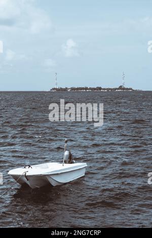 Une superbe photo verticale d'un bateau de pêche blanc attaché à un autre bateau, tandis que l'eau de mer et une île pittoresque dominent le backgr Banque D'Images