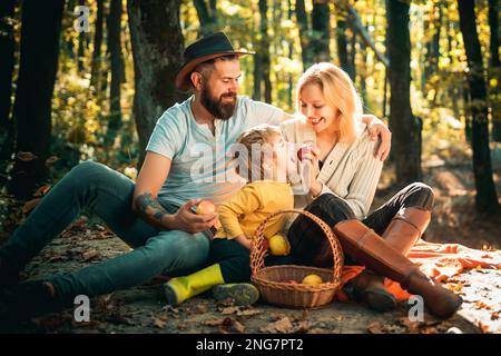 Panier avec repas de pique-nique et jouets pour les enfants. Une famille heureuse de trois personnes se trouvant dans l'herbe en automne. Le concept d'une famille heureuse. Jeune famille souriante Banque D'Images