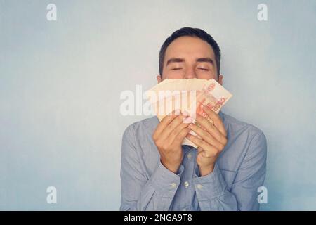 Homme sniffing dollars. La douce odeur de l'argent. Un jeune gars qui a renifé 5000 roubles a gagné de l'argent. Salaire. Argent facile. Un paquet d'argent Banque D'Images