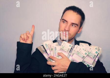 guy dans le costume et l'argent dans ses mains pointe son doigt vers le haut. Jeune homme sur le mur gris de grunge, numéro un. Bonne idée d'affaires Banque D'Images