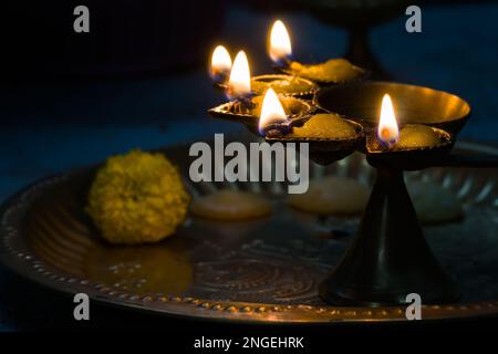 un panch hindu puja essential pradeep ou une lampe à huile à cinq têtes qui brûlent avec une flamme éclatante et des fleurs marigolées gardées sur une plaque en laiton. ils sont utilisés dans dur Banque D'Images