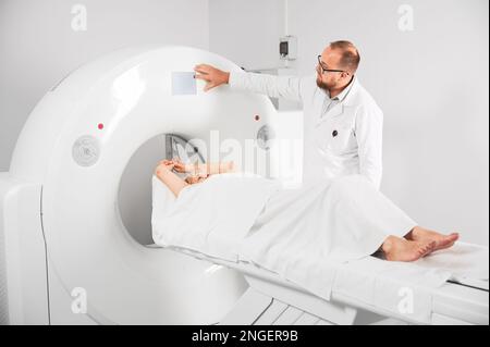 Scanner médical de tomodensitométrie ou IRM. Un radiologue appuie sur le bouton IRM pour examiner une patiente. Banque D'Images