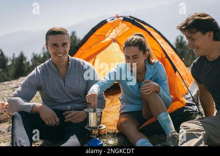 Gros plan de trois amis souriant et faisant du café tout en étant assis devant la tente Banque D'Images