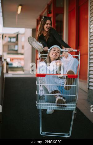 Les filles avec le chariot de marché ayant le plaisir tandis que l'un d'eux conduit le chariot l'autre est en lui Banque D'Images