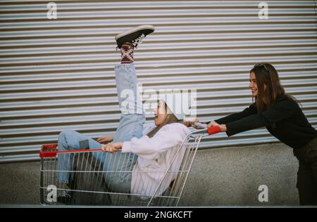 Deux belles filles ayant l'amusement pendant qu'elles conduisent un chariot l'autre je m'asseyant dans lui Banque D'Images