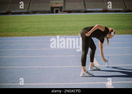 Une jogging femelle laisse la bouteille d'eau sur la piste sportive, après qu'elle ait bu Banque D'Images
