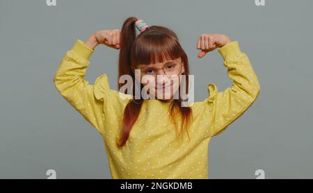 Je suis fort et en bonne santé. Jeune fille en lunettes montrant biceps et regardant confiant sentir la force de puissance de lutter pour les droits, l'énergie pour gagner la réussite gagner. Enfant préadolescent sur fond gris Banque D'Images