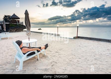 Détendez-vous dans un transat, à côté d'une plage tropicale, en regardant le soleil doré se coucher derrière des nuages qui s'ensuivent, à travers la mer des Philippines, se sentant calme et Banque D'Images