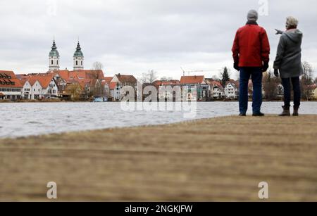 Bad Waldsee, Allemagne. 18th févr. 2023. Un couple se tient sur une passerelle en bois au lac de la ville et regarde dans la direction de l'église paroissiale de Sankt Peter crédit: Thomas Warnack/dpa/Alamy Live News Banque D'Images