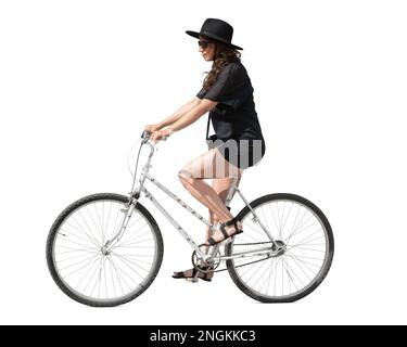Jeune femme vêtue d'une robe noire et portant un chapeau noir à cheval sur un vélo isolé sur fond blanc Banque D'Images