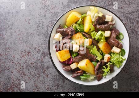 Salade gastronomique avec gésiers et pommes de terre frites dans une assiette sur la table. Vue horizontale du dessus Banque D'Images