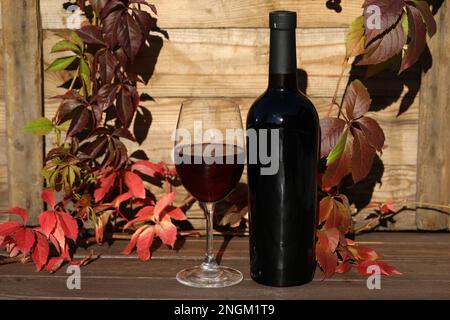 verre de vin rouge sur fond de bois avec feuilles d'automne et bouteille Banque D'Images